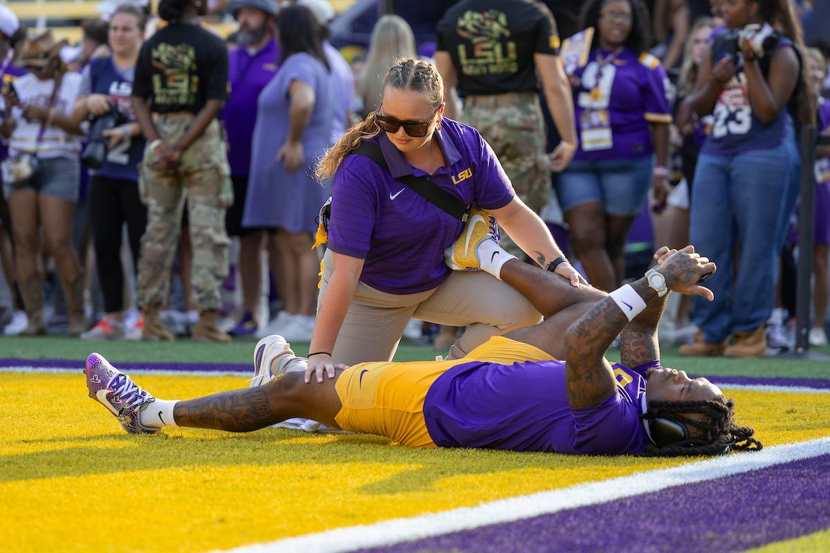 Student athletic trainer helps stretch a football player